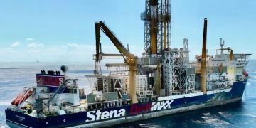 Offshore drilling ship at sea, blue hull with 'Stena Drilling' branding and tall yellow derricks towering above.