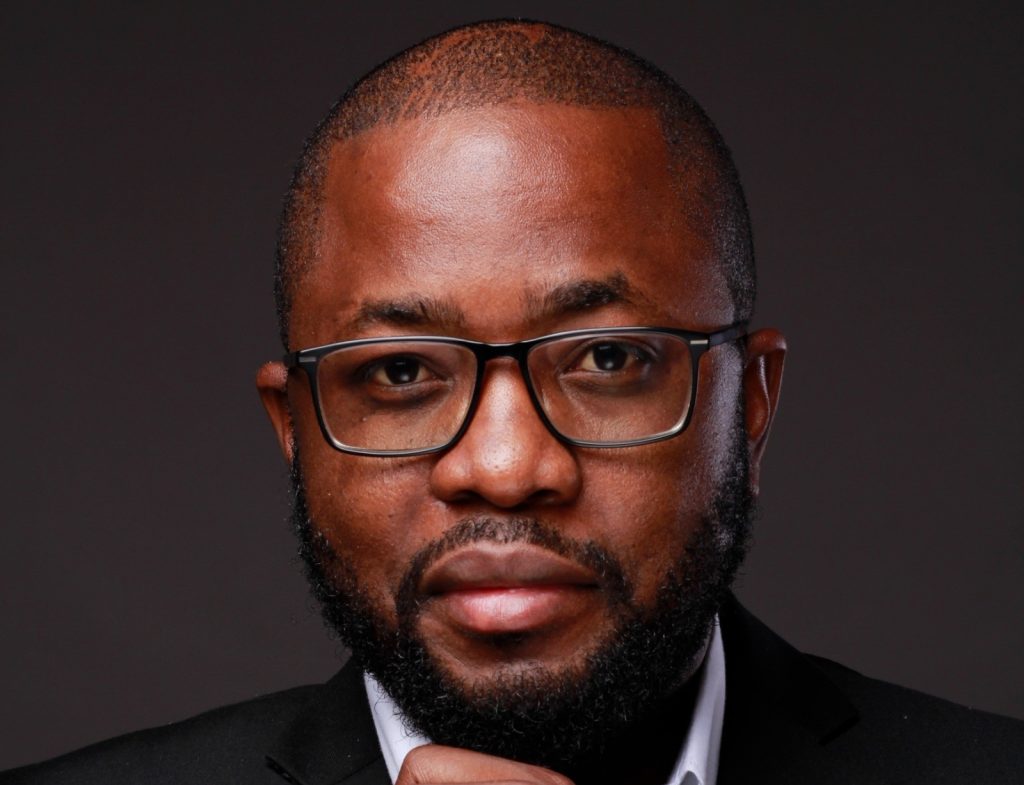 LOT | Mining and Energy Namibia | Namibia’s Leading Mining & Energy News Close-up portrait of a man with glasses and a beard, wearing a dark suit against a dark background.