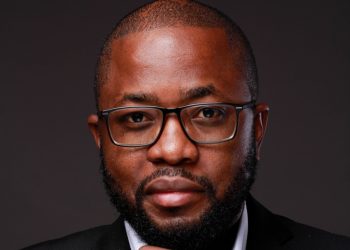 LOT | Mining and Energy Namibia | Namibia’s Leading Mining & Energy News Close-up portrait of a man with glasses and a beard, wearing a dark suit against a dark background.
