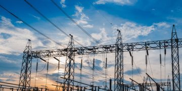 Electrical substation with metal towers and power lines silhouetted against a sunset sky, cables crisscrossing overhead.