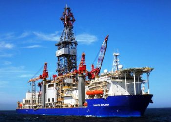 Offshore drilling ship Tungsten Explorer with tall derrick and red cranes at sea under a blue sky