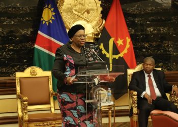WhatsApp Image 2026-10-22 at 114822 3 | Mining and Energy Namibia | Namibia’s Leading Mining & Energy News Woman in colorful patterned outfit giving a formal speech at a podium with two flags behind her and a man seated nearby on a golden chair in a formal hall