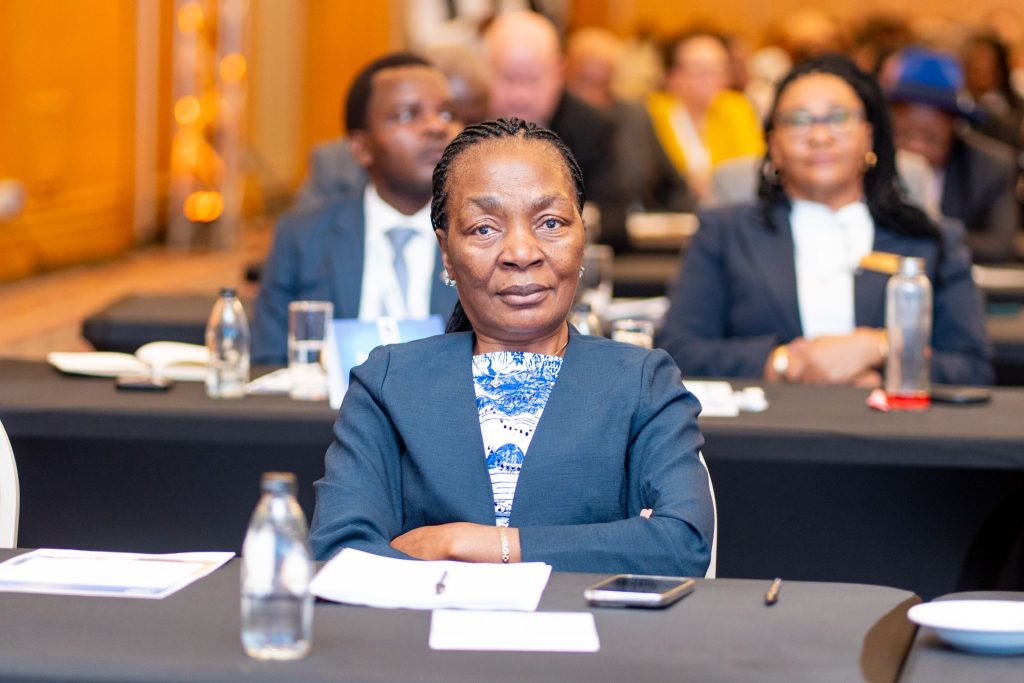 Ericah Shafudah NamPPF | Mining and Energy Namibia | Namibia’s Leading Mining & Energy News Front-on portrait of a professional woman in a blue blazer sitting at a conference table, with a blurred audience in the background.