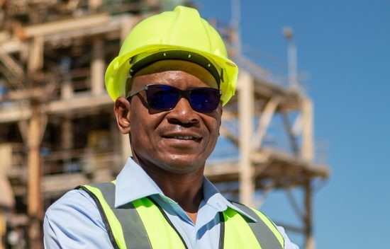 GEORGE BOTSHIWE1 | Mining and Energy Namibia | Namibia’s Leading Mining & Energy News Construction worker wearing a neon yellow hard hat and safety vest at a building site with scaffolding in the background.