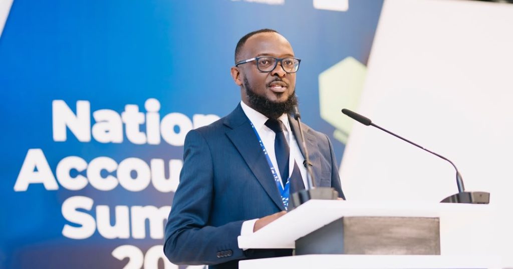 WhatsApp Image 2026-10-23 at 121601 PM | Mining and Energy Namibia | Namibia’s Leading Mining & Energy News Man in a navy suit and glasses speaks at a podium during a conference, blue backdrop reading 'National Accounts Summit' behind him.