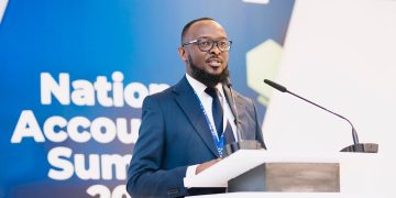 WhatsApp Image 2026-10-23 at 121601 PM | Mining and Energy Namibia | Namibia’s Leading Mining & Energy News Man in a navy suit and glasses speaks at a podium during a conference, blue backdrop reading 'National Accounts Summit' behind him.