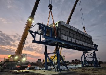 hydrogen 5 | Mining and Energy Namibia | Namibia’s Leading Mining & Energy News Two large cranes lift stacked concrete blocks onto a blue steel platform at a construction site during sunset.